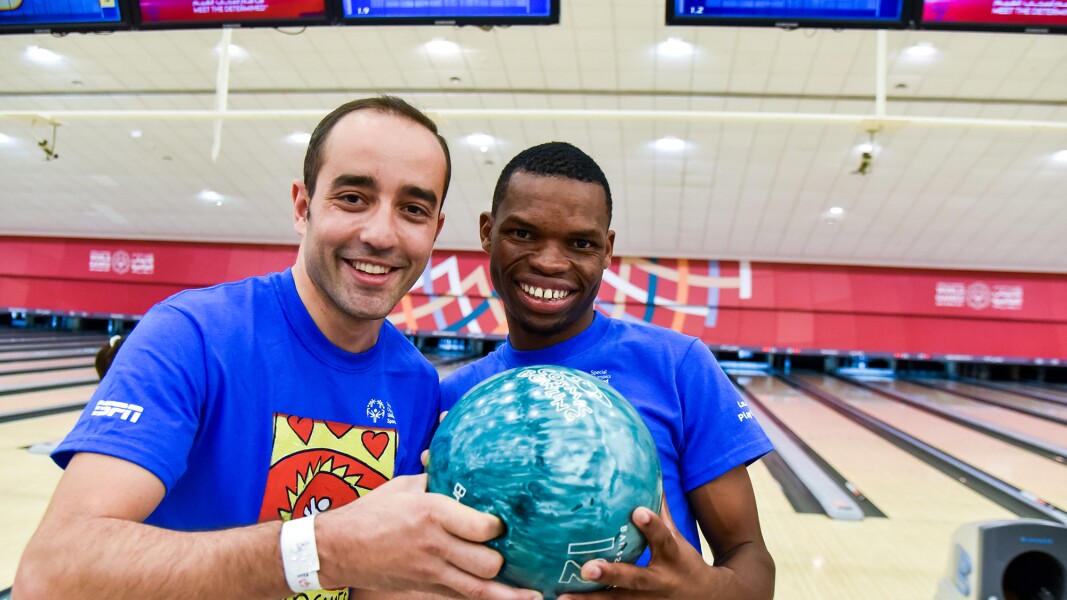 Zwei Bowling-Spieler lächeln in die Kamera und halten gemeinsam eine Bowlingkugel.