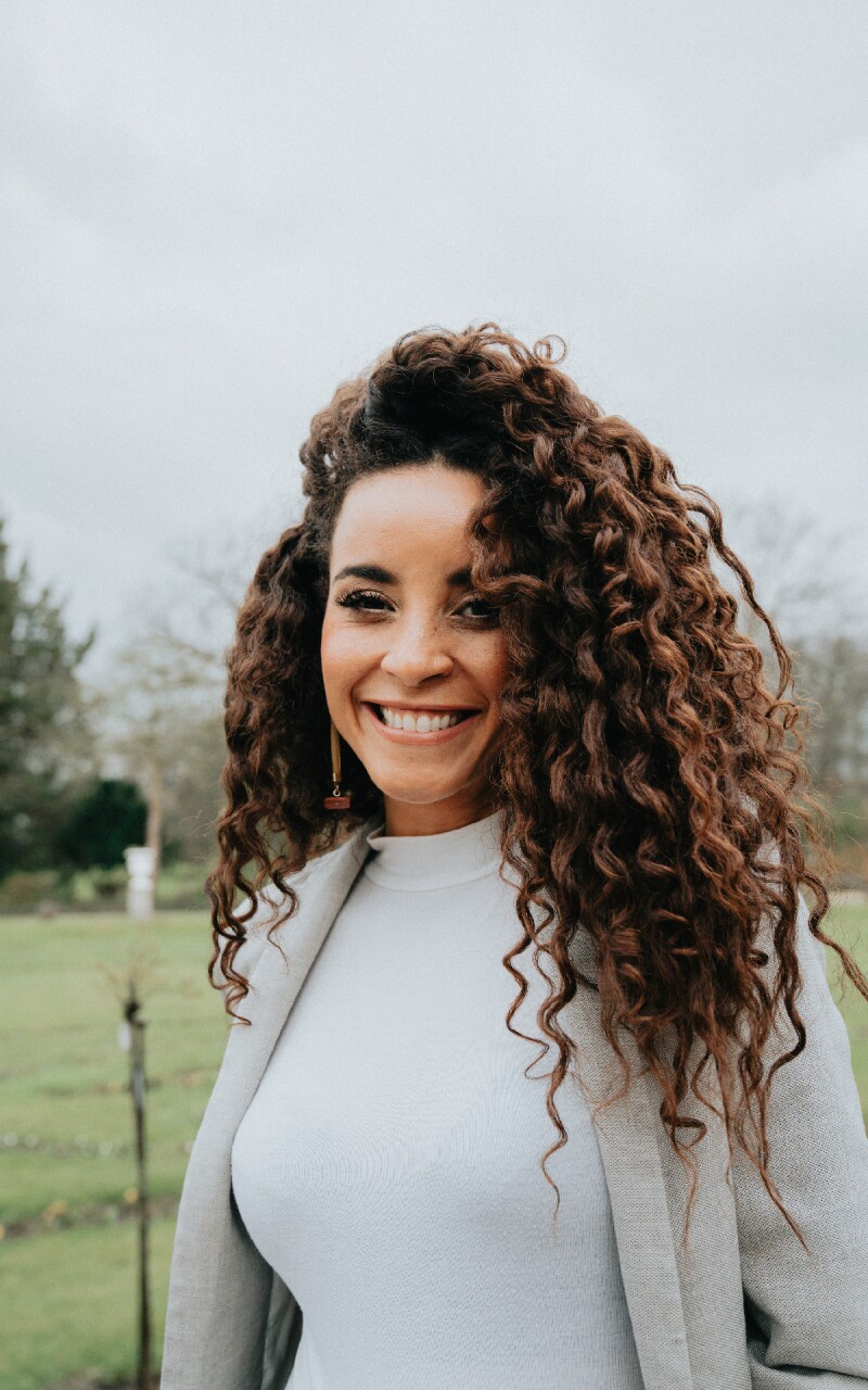 Auf dem Foto sieht man die Miss Germany 2022 Domitila Barros. Sie trägt ein schlichtes weißes Outfit und lächelt in die Kamera.