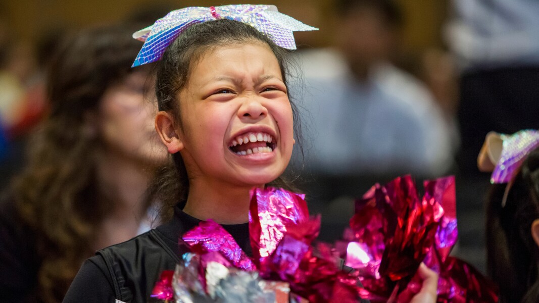 In the photo a cheerleader is happy. She has pompoms in her hand.
