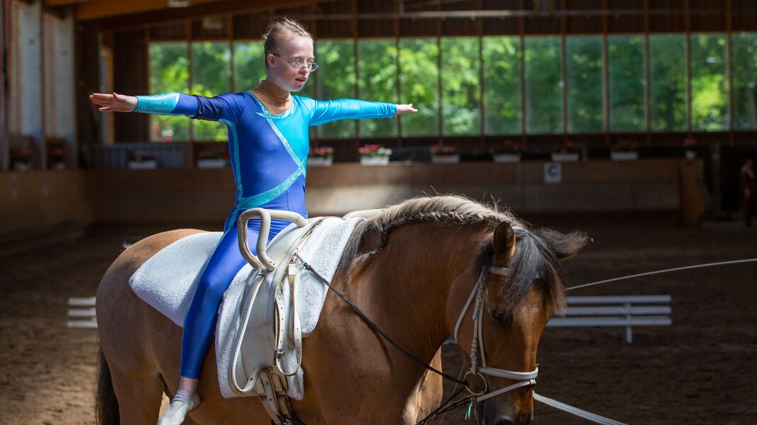 On the photo there is an athlete performing her vaulting choreography. She has her arms spread widely and looks concentrated.