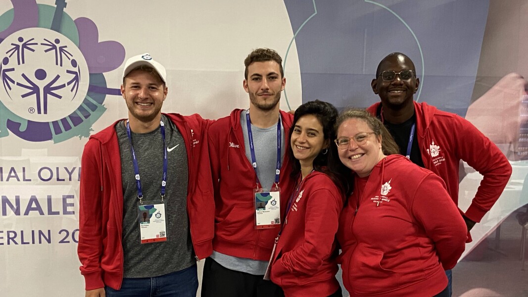 On the photo, there are five corporate volunteers standing in front of a Special Olympics National Games Berlin 2022 banner, smiling towards the camera and wearing volunteer clothes.