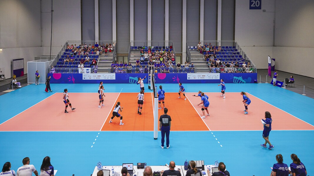 Das Foto zeigt eine Szene beim Volleyball. Die Halle ist fast in kompletter Größe dargestellt und das Spiel ist im vollen Gange. Im Hintergrund ist das Publikum.