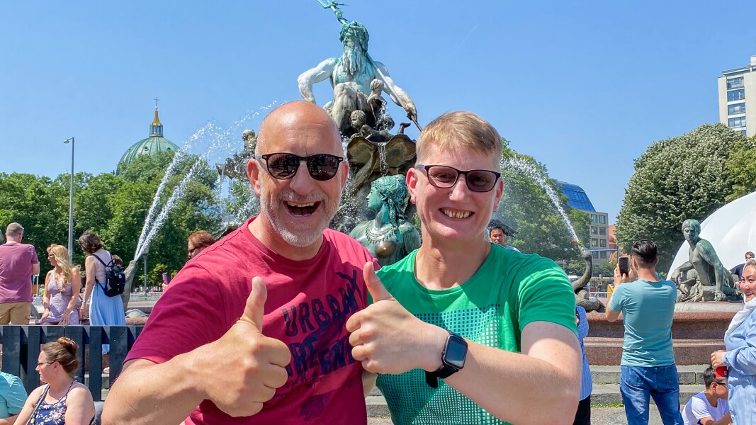 On the photo, there are two people smiling and showing their thumbs up. They are standing in front of Neptunbrunnen where the Special Olympics Festival took place during the National Games, and where is will be hosted again during the World Games Berlin 2023.