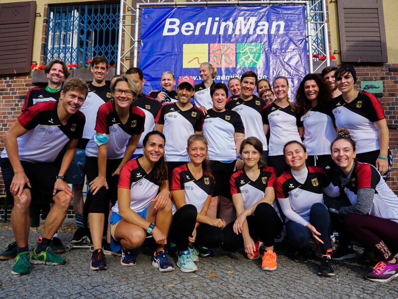 Alle+Teilnehmer_innen+des+Triathlons+posieren+gemeinsam+und+mit+Freude+vor+dem+blauen+BerlinMan-Banner.jpeg