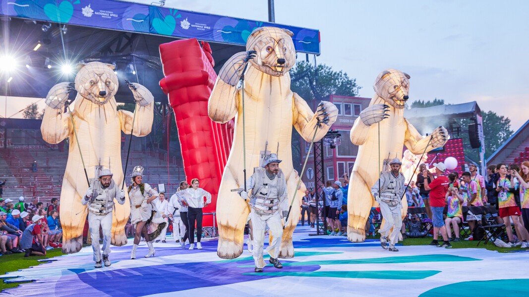 Auf dem Bild sieht man eine Performance während der Eröffnungsfeier der Nationalen Spiele mit aufgeblasenen Bären und dem Brandenburger Tor im Hintergrund.