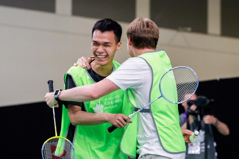 On the picture two athletes hugging and smiling playing badminton.
