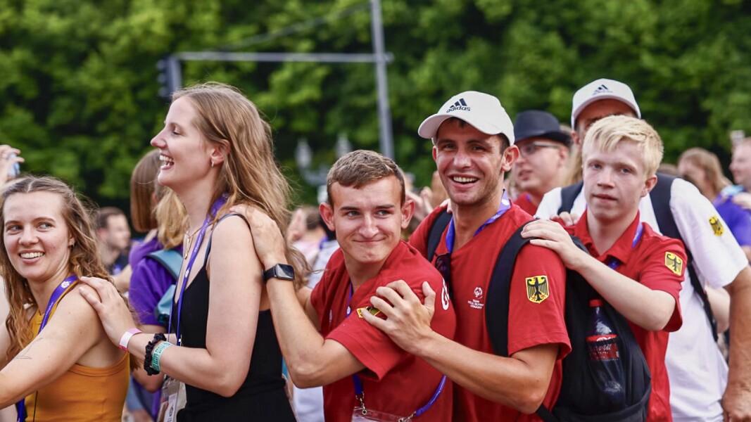 Das Foto zeigt Athleten und Volunteers in einer Polonaise. Darunter sind drei junge Männer eines deutschen Teams. Alle Personen lachen.