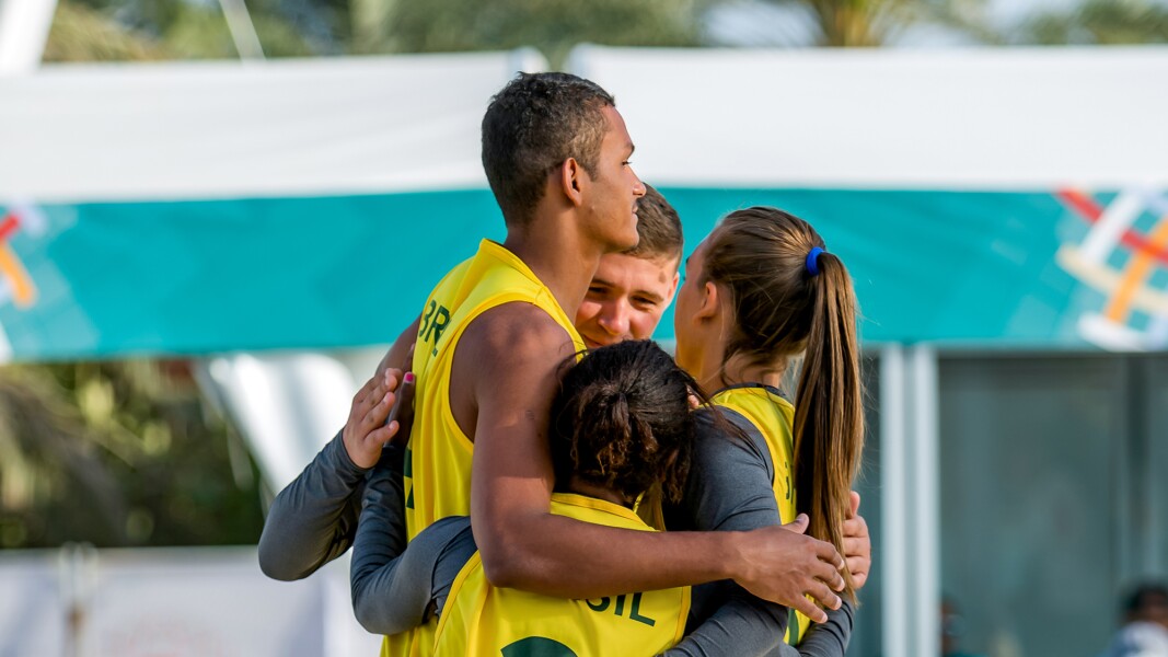 Das Foto zeigt vier Beachvolleyball-Spieler*innen, die gerade zusammen stehen und sich gegenseitig umarmen.