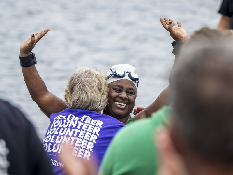 In the photo, a female open water swimmer is cheering after her race. At the same time, she is warmly embraced by a volunteer.