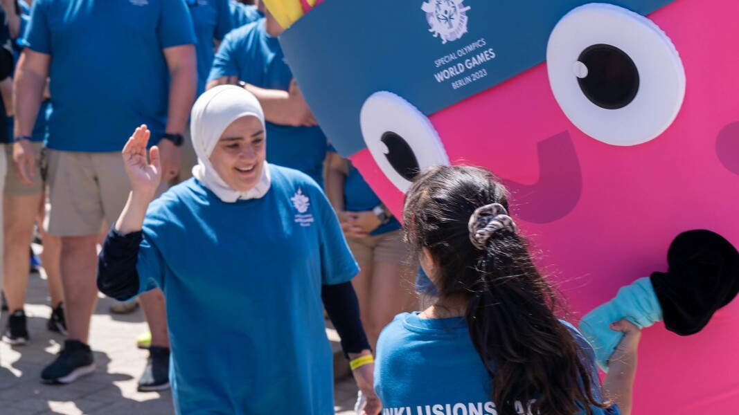 Das Foto zeigt zwei Athletinnen der Delegation aus Syrien, die gerade das Maskottchen Unity im Rahmen des Host Town Programs treffen.