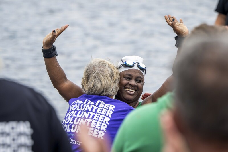 In the photo, a female open water swimmer is cheering after her race. At the same time, she is warmly embraced by a volunteer.