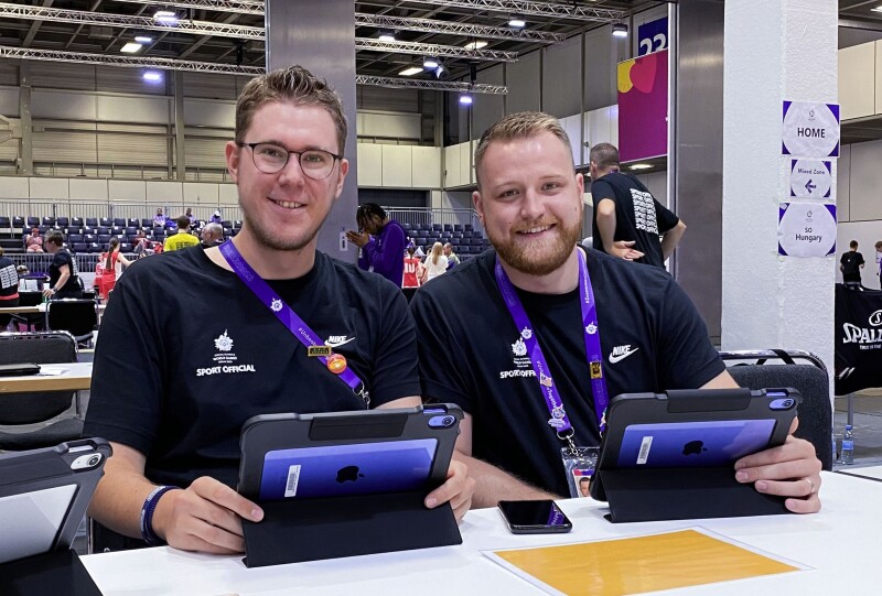 Das Foto zeigt die beiden Unified Observer Felix Beiser und Kilian Wich bei ihrer Arbeit beim Basketball. Beide halten ein Tablet in der Hand und lächeln freundlich.