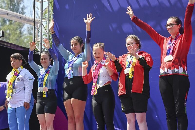 Auf dem Bild stehen 6 Athetinnen auf dem Podium und freuen sich auf über die gewonnen Medaillen. Alle jubeln vor Freude mit gestreckten Armen nach oben in Richtung des Publikums.