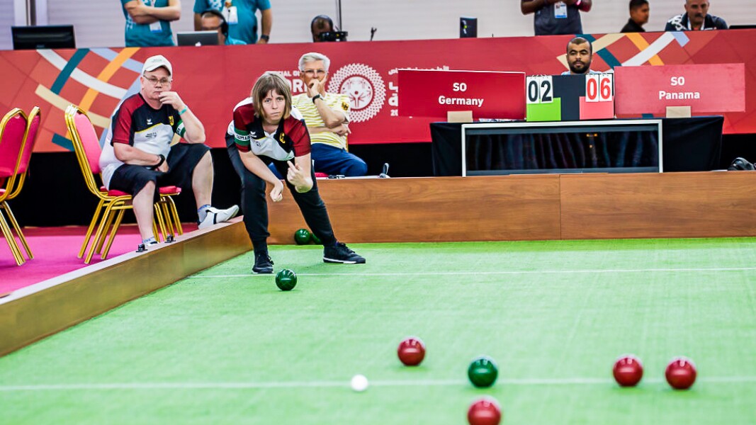 Auf dem Bild ist eine Athletin beim Boccia spielen zu sehen. Im Vordergrund sind außerdem die Kugeln und im Hintergrund der Spielstand.