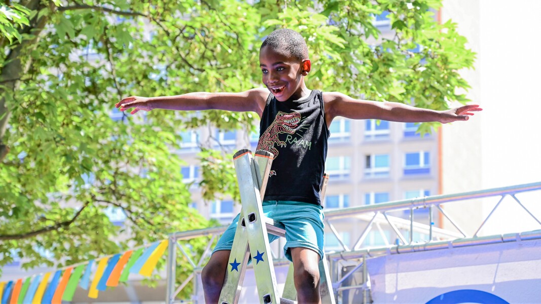 Das Foto zeigt einen jungen, der bei einer Station des Special Olympics Festivals mitmacht. Er sitzt auf einer Leiter, hat die Arme ausgebreitet und lacht vergnügt.