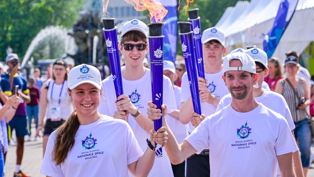 Auf dem Foto sind die Gesichter der Spiele Lilly Binder und Robert Herberg zu sehen, die gemeinsam die "Flamme der Hoffnung" tragen und dabei stolz lächeln.