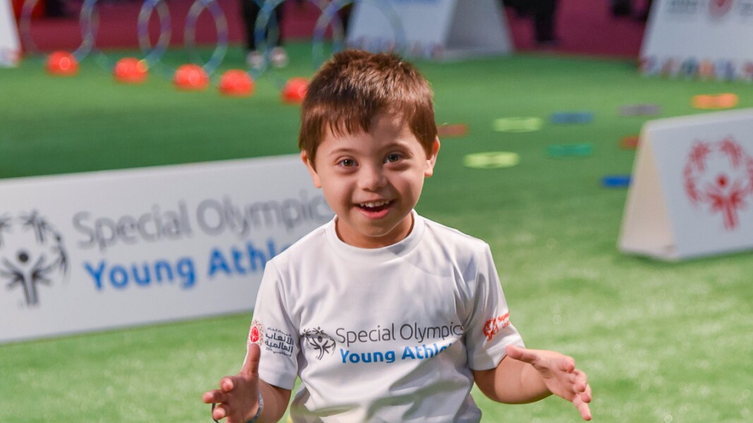Auf dem Foto steht ein Junge lachend auf einer bunten Balancier-Schlange, die Teil des Young Athletes Programms ist.