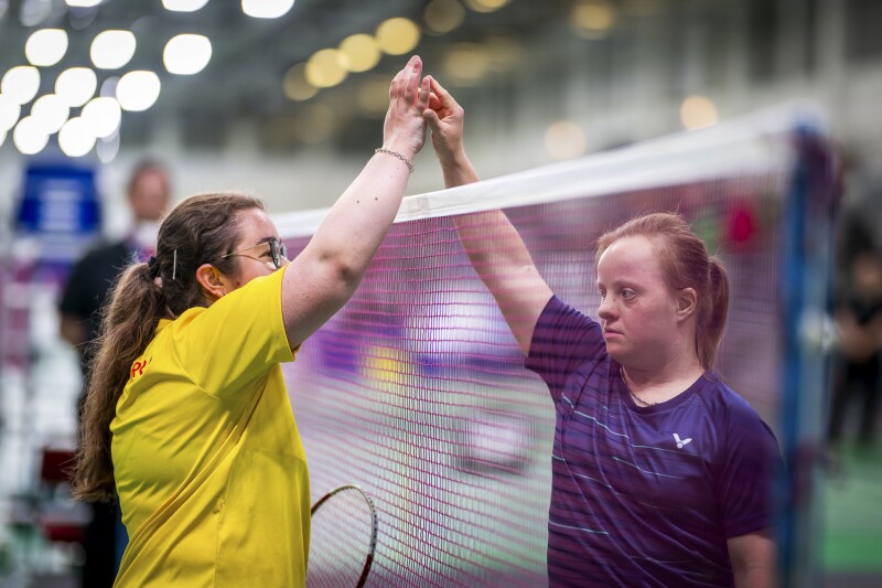 Auf dem Foto klatschen zwei gegnerische Spielerinnen über dem Badminton-Netz ab.
