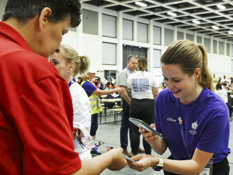The photo shows a volunteer scanning an athletes' IDs at lunch. She is smiling as she does this.