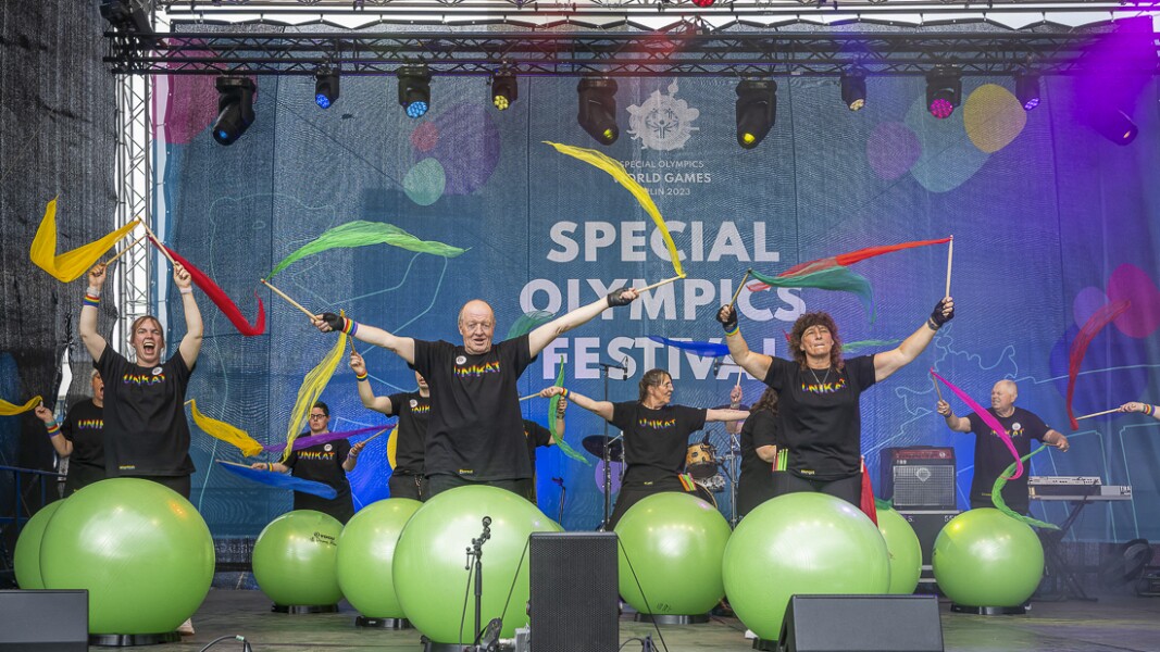 In the photo there are several performers on the stage. They are waving flags. All of them are in a good mood.