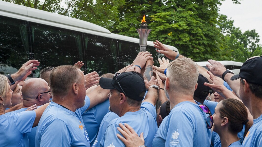 The photo shows participants of the torch run. They are all stretching their hands towards the torch.