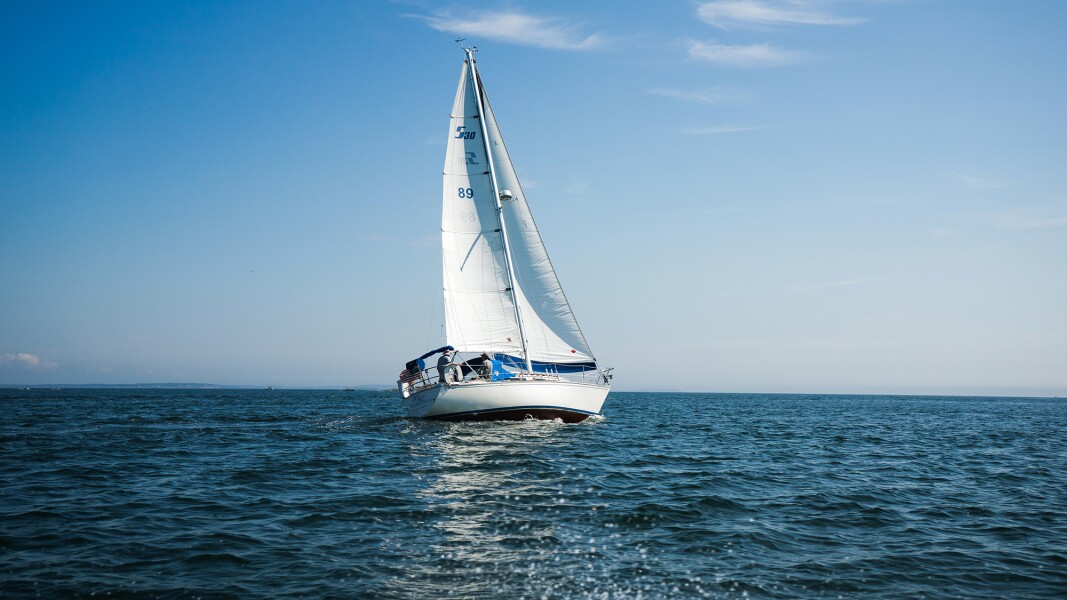 Das Foto zeigt eine malerische Szene auf dem Meer: ein Segelboot vor blauem Himmel.