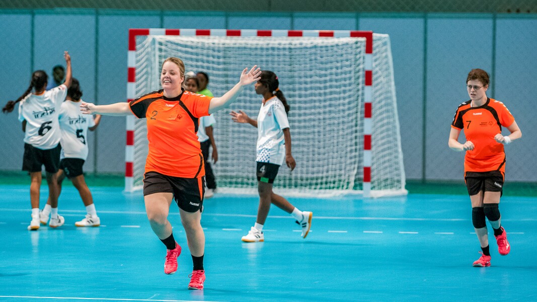 Das Foto zeigt zwei Mannschaften beim Handball. Eine Sportlerin streckt die Arme aus.