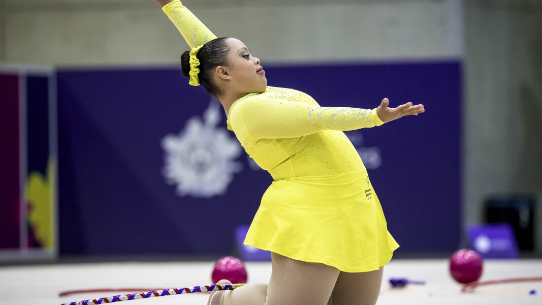 in this picture a girl is wearing yellow color leotard while peforming her Stunt where as her right hand is showing towards crowd and her left hand is facing up
