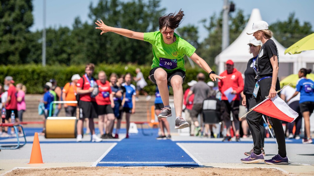 The photo shows five runners* competing. They are running and are cheered by numerous fans.