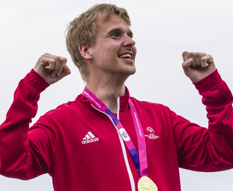 Das Foto zeigt Kai-Jürgen Pönisch von TeamSOD nachdem er seine Goldmedaille im Freiwasserschwimmen bekommen hat. Er hat die Arme erhoben und jubelt lächelnd. 