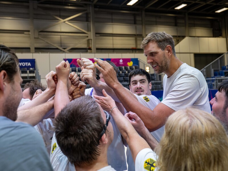 Dirk Nowitzki steht im Kreis mit den Spielern des Deutschen Basketballteams. Sie halten zusammen die Hände in die Mitte.