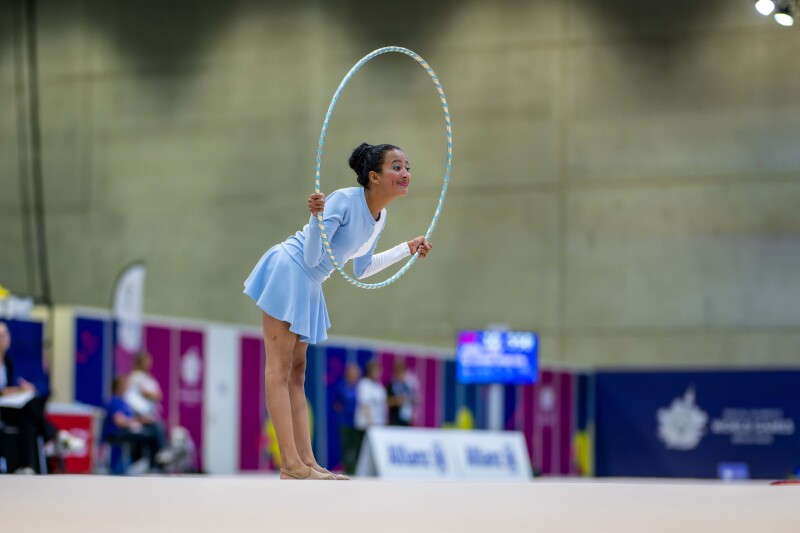 The photo shows a female athlete of rhythmic gymnastics with a sports gymnastics hoop. She smiles at the spectators.