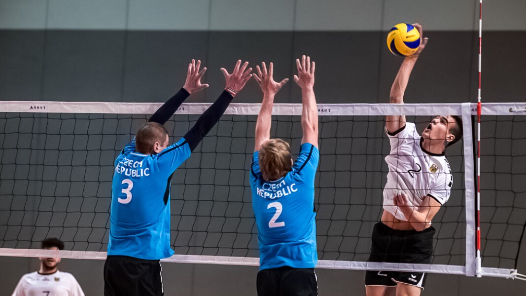 Das Foto zeigt eine Spielszene beim Volleyball: zwei Spieler versuchen zu blocken und der gegenerische Spieler macht gerade einen Angriffsschlag.