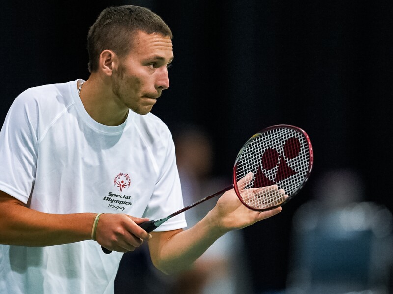 The photo show a concentrated Badminton player during competition. He has a racket in his hand.