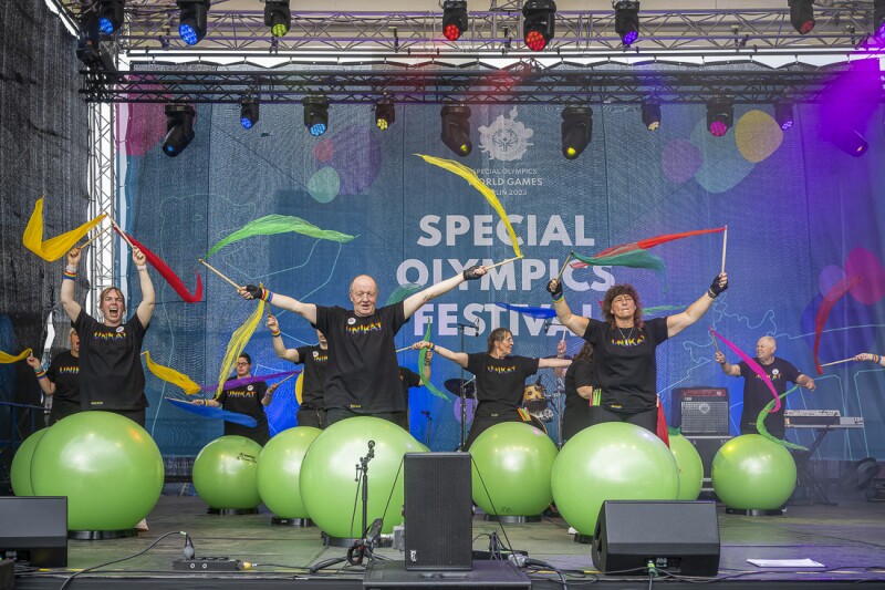 In the photo there are several performers on the stage. They are waving flags. All of them are in a good mood.