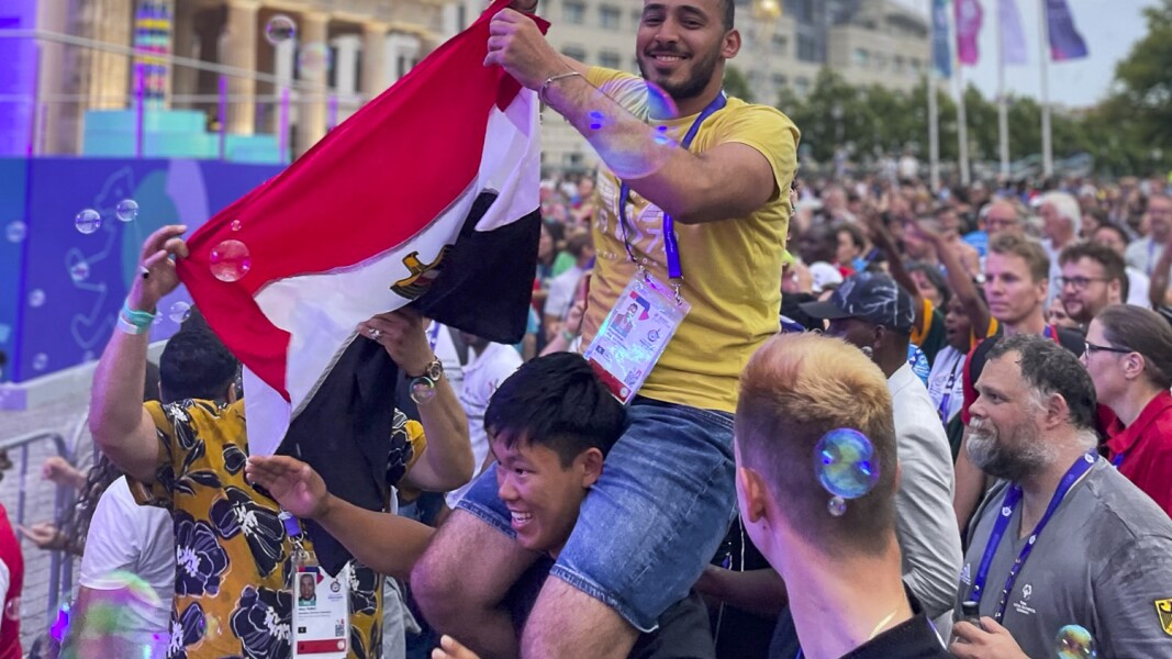 The photo shows celebrating men in front of the stage of the athletes' party. A man with an Egyptian flag in his hand sits on the shoulders of another man.