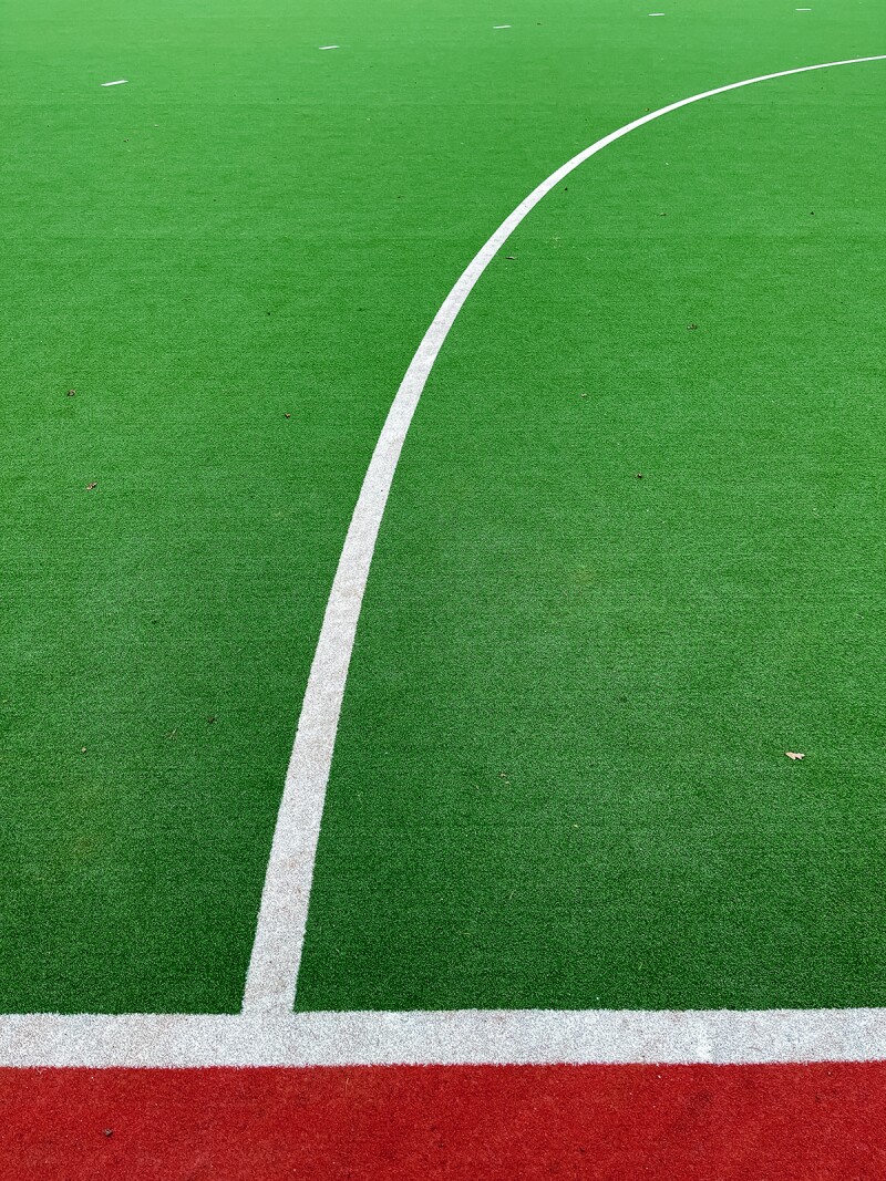 The photo shows the grass and lines of a Hockey pitch. 