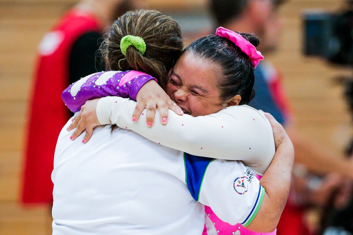 In the photo, two female athletes are hugging each other. They laugh and are happy.