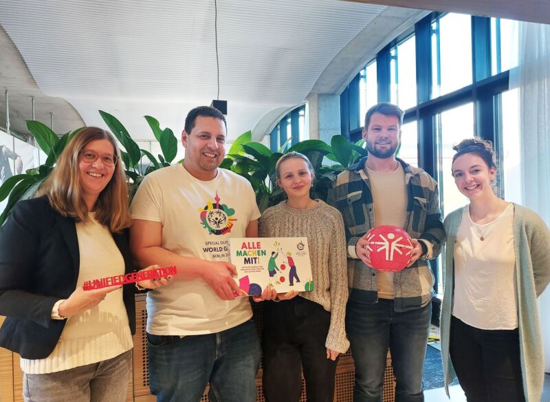 Das Foto zeigt 5 Mitarbeitende aus dem Weltspieleteam, die alle am Aktionspaket "Alle machen mit!" gearbeitet haben und das Ergebnis stolz präsentieren. Das nachhaltige Ziel davon ist, Schulen und Kitas langfristig inklusiver zu machen.