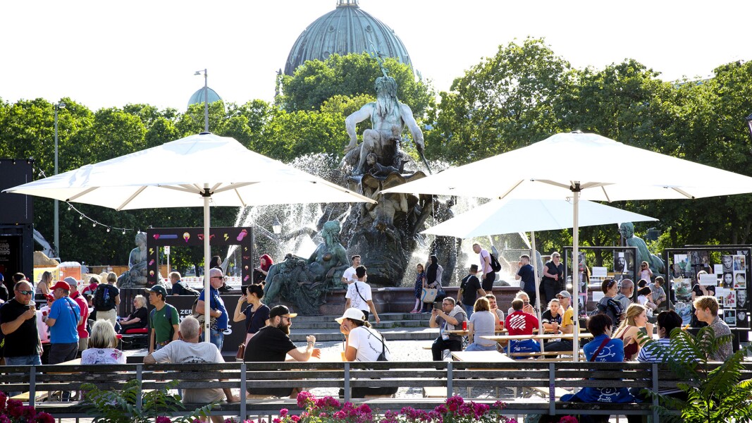 The photo shows a scene of the Special Olympics Festival directly at the famous Neptune Fountain next to Alexanderplatz in the heart of Berlin. Many people are either strolling by or sitting relaxed on benches.