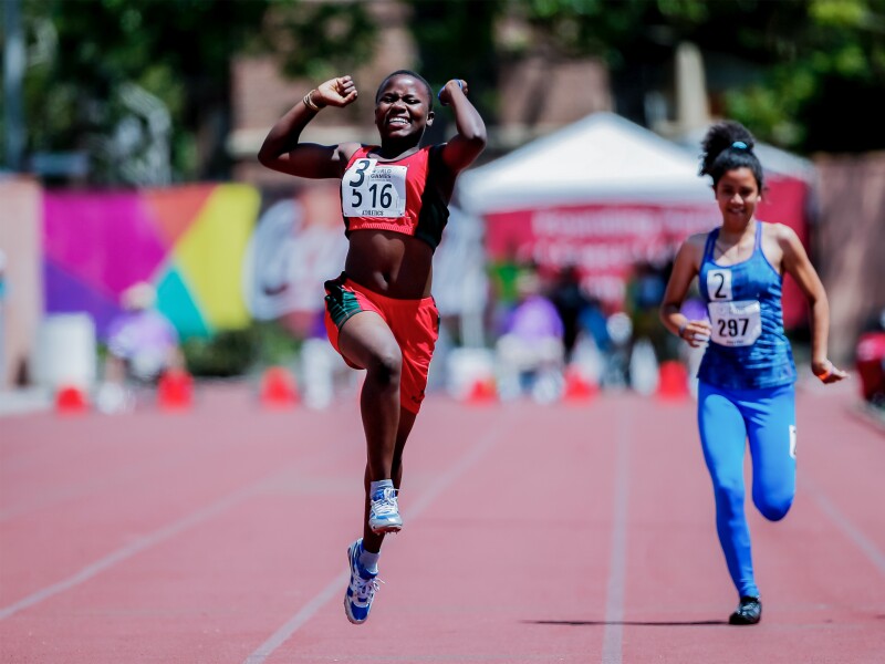 The photo shows two athletes on the track. One is ahead and already starts to cheer as she is winning.