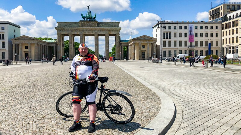 The photo shows Special Olympics Germany athlete Dennis Mellenthin with his bicycle in front of the Brandenburg Gate.