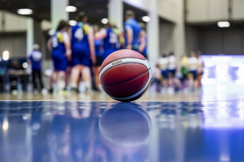 A basketball laying on the blue court with players in the background