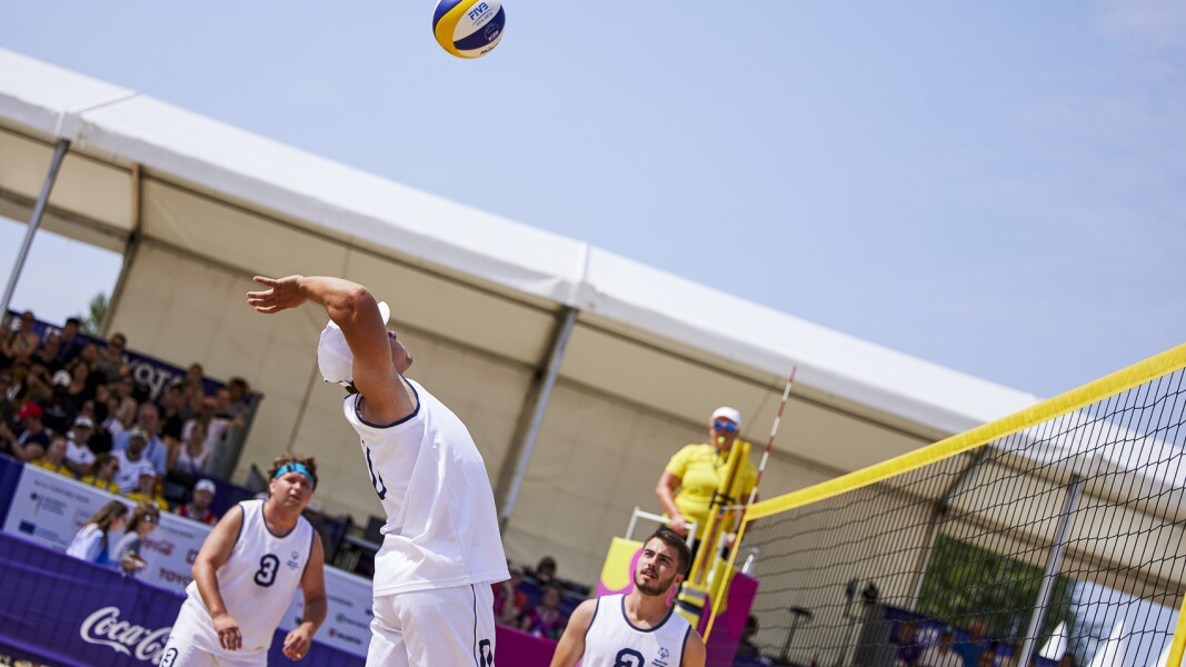 Ein Spieler der serbischen Beach Volleyball-Mannschaft holt nach hinten gebeugt zum Schlag über das Netz aus.