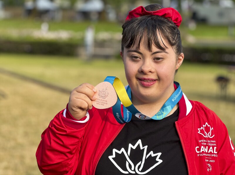 Das Foto zeigt eine Athletin der Rhythmischen Sportgymnastik mit ihrer Medaille in der Hand. Sie lächelt in die Kamera. 