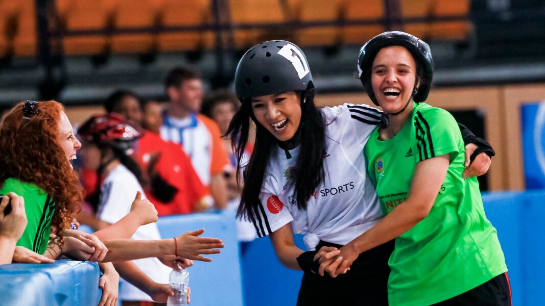 Zwei Athletinnen haben Spaß beim Roller Skating und halten sich gegenseitig.