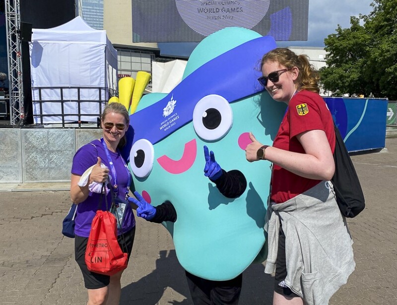 The photo shows two women with the mascot Unity. They are pointing their thumbs up and smiling. 