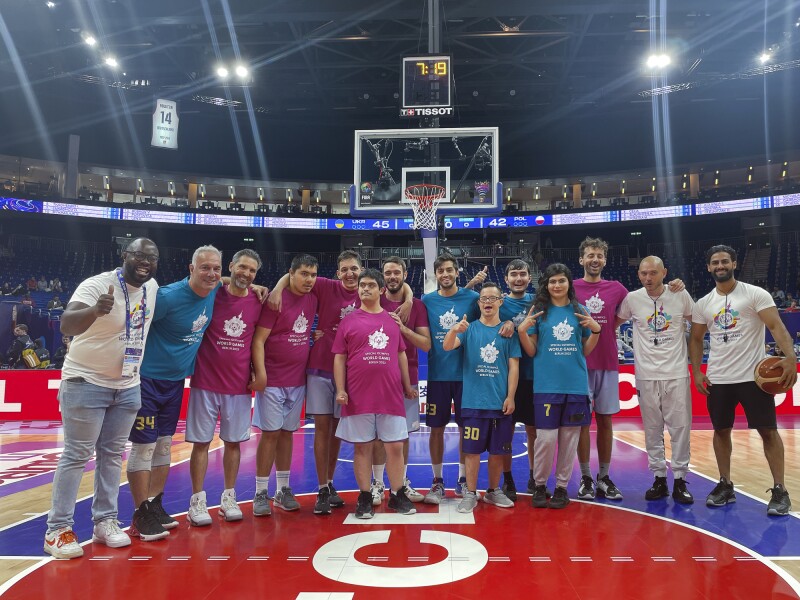 Das Foto ist ein Gruppenbild der Spieler*innen von Mina Basket auf dem Main Court der Basketball Europameisterschaft in Berlin, wo sie ein Halbzeit-Show-Match spielen durften. Das Unified Basketball Team liegt sich in den Armen und alle lächeln freudig in Richtung Kamera.