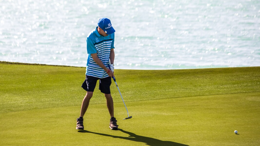 Das Foto zeigt einen Golfer der auf dem Rasen steht und gerade einen Ball abgeschlagen hat. Im Hintergrund ist ein See zu sehen.
