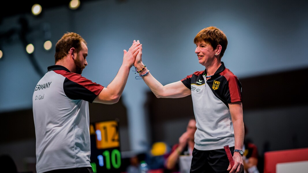 Das Foto zeigt zwei Badminton-Spieler*innen, die sich gerade ein High-Five auf dem Spielfeld geben.